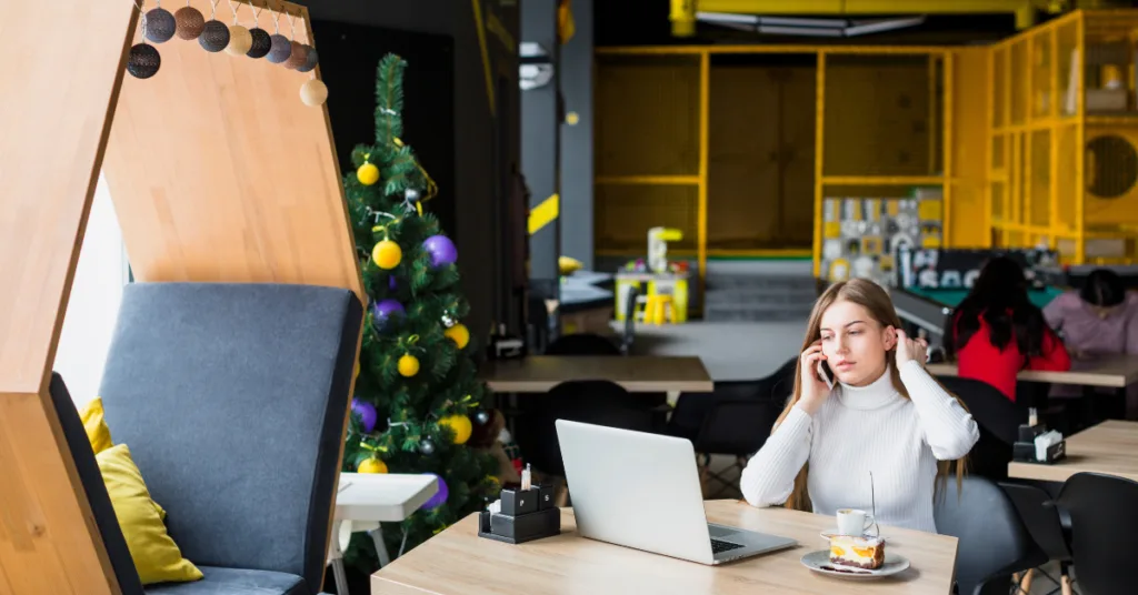 A modern coworking space featuring a cozy wooden seating area, a Christmas tree, and a professional working on a laptop while talking on the phone.